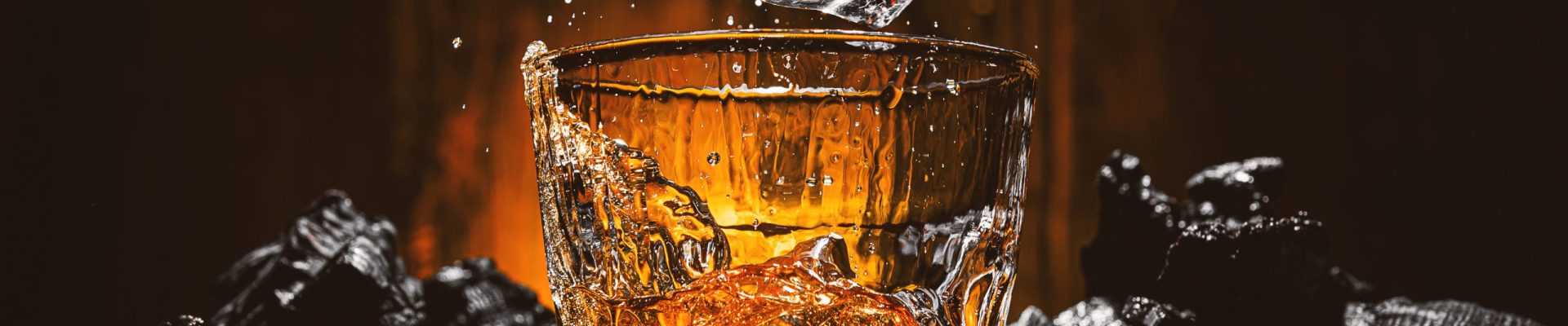 ice cubes fall into a glass with a brown alcoholic drink ice cubes fall into a glass with a brown alcoholic drink. splashes from falling ice fly in different directions