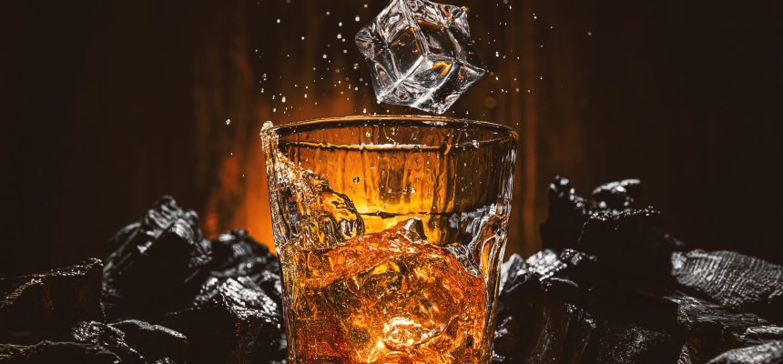 ice cubes fall into a glass with a brown alcoholic drink ice cubes fall into a glass with a brown alcoholic drink. splashes from falling ice fly in different directions