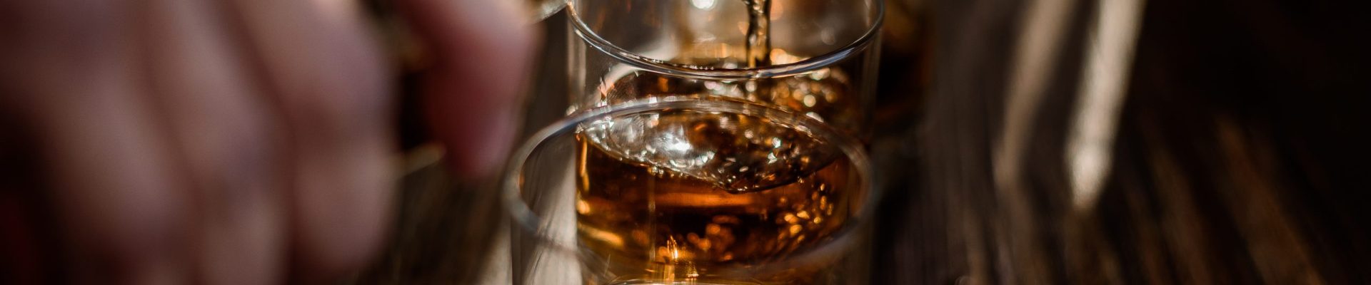 Pouring strong alcohol drink into the glasses which are on the w Pouring strong alcohol drink into the glasses which are on the wooden table
