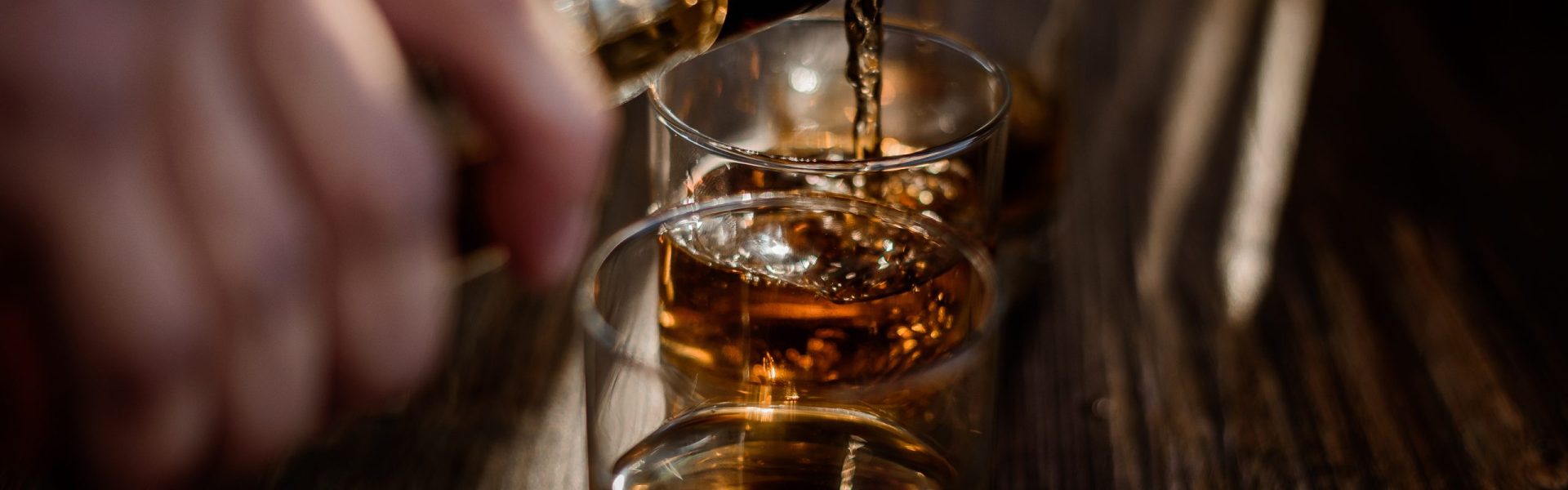 Pouring strong alcohol drink into the glasses which are on the wooden table